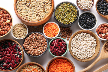 Composition with bowls of different raw legumes on white background