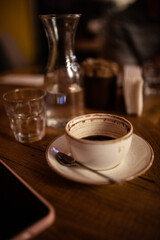 Cup of coffee on the wooden table in cafe. Glass bottle of water. Dark mood