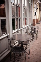 A charming english cafe with wicker chairs and tables set out on a cobblestone sidewalk on a drizzly day. The warm glow of the interior lights contrasts with the cool tones of the street