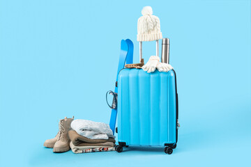 Suitcase with winter accessories and skis on blue background