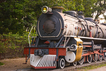 A vintage steam locomotive in motion, with thick smoke billowing from the chimney. The powerful machine is captured on the tracks, evoking a sense of nostalgia and industrial history.