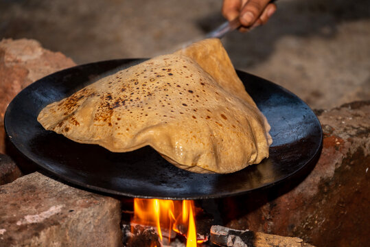 A village woman makes bread on the stove. cooking bread in clay stove , chula , makeing bread , roti , in village