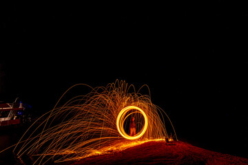 Creative fire spinning creates dazzling light trails at night along the beach