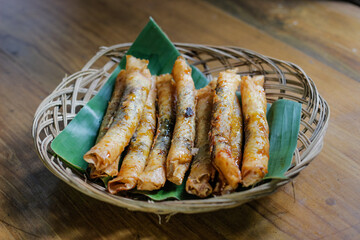 photo of serving aromatic banana snack or layered banana on a wicker plate lined with fresh green banana leaves on varnished wood. photo taken from a high angle