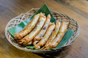 photo of serving aromatic banana snack or layered banana on a wicker plate lined with fresh green banana leaves on varnished wood. photo taken from a high angle