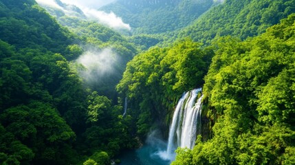 Fototapeta premium A breathtaking waterfall cascades through lush green forests, surrounded by misty mountains, showcasing the beauty of nature.