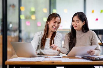 Obraz premium Two asian confident business people point to graphs and charts to analyze market data, balance sheet, account, net profit to plan new sales strategies to increase production capacity. 
