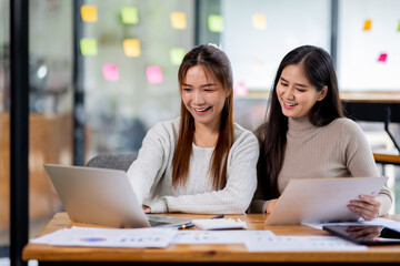 Two asian confident business people point to graphs and charts to analyze market data, balance sheet, account, net profit to plan new sales strategies to increase production capacity.	
