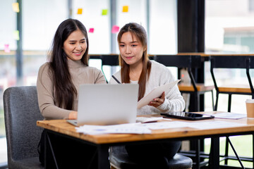 Two asian confident business people point to graphs and charts to analyze market data, balance sheet, account, net profit to plan new sales strategies to increase production capacity.	
