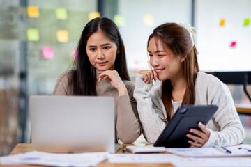 Two asian confident business people point to graphs and charts to analyze market data, balance sheet, account, net profit to plan new sales strategies to increase production capacity.	
