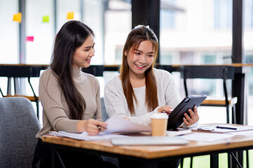 Fototapeta premium Two asian confident business people point to graphs and charts to analyze market data, balance sheet, account, net profit to plan new sales strategies to increase production capacity. 