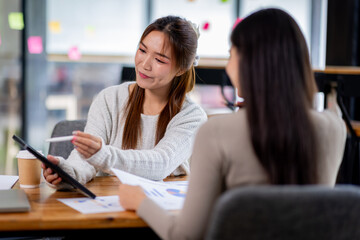 Two asian confident business people point to graphs and charts to analyze market data, balance sheet, account, net profit to plan new sales strategies to increase production capacity.	
