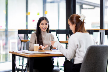 Fototapeta premium Two asian confident business people point to graphs and charts to analyze market data, balance sheet, account, net profit to plan new sales strategies to increase production capacity. 