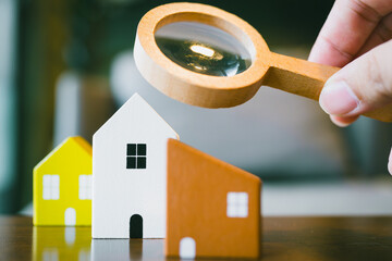 Hand holding magnifying glass and looking at house model, house selection, real estate concept.