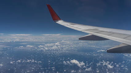 Obraz premium The airliner is in flight. An airplane wing on a blue sky background. The ocean is below. Cumulus clouds are reflected in the water. Malaysia.