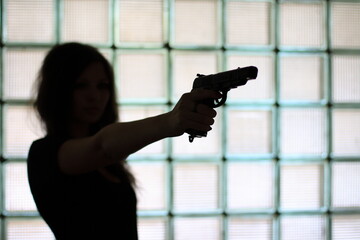 Silhouette of a woman with a gun on a glass wall background.