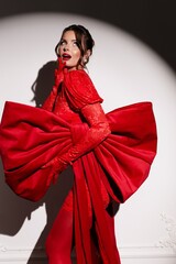 Elegant brunette in red dress with lush red bow, captured in dramatic studio spotlight for fashion theme.