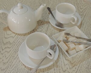 white ceramic tea set on light textured wooden tabletop, two mugs, teapot and sugar bowl as still life for tea party