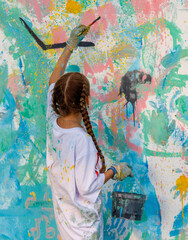 A girl is painting a wall with a bucket of paint