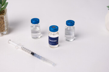 top view of some vaccines and a syringe with artificial flowers on a table, inside a clinic room. health and medical concepts