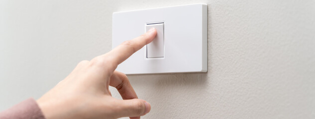 Save energy concept, Close-up finger of people turning off the electrical light switch on the wall before leaving home for security safety and save electricity bills expenses.
