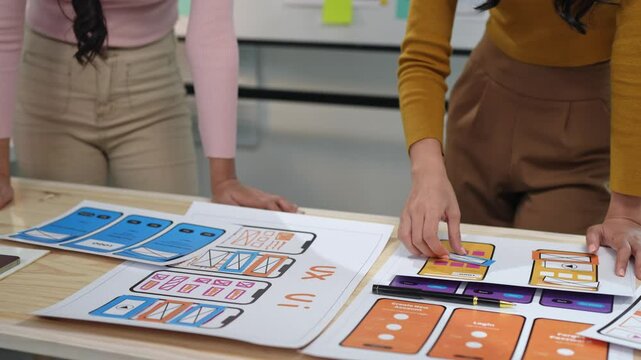 Two female designers design creative UX UI screen for mobile responsive application development, developing mockup wireframe on smartphone screen, application development team, brainstorming.