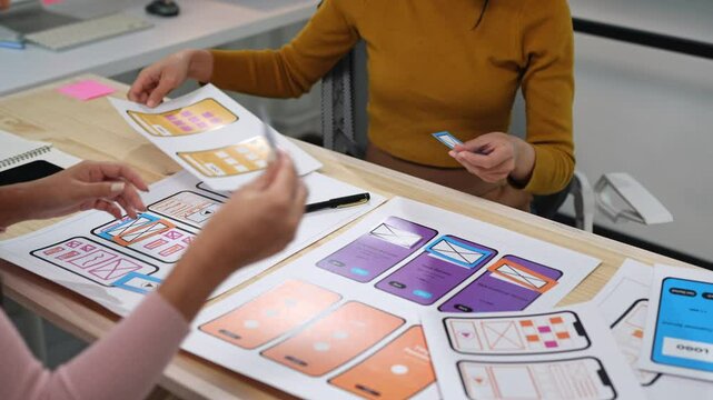 Two female designers design creative UX UI screen for mobile responsive application development, developing mockup wireframe on smartphone screen, application development team, brainstorming.