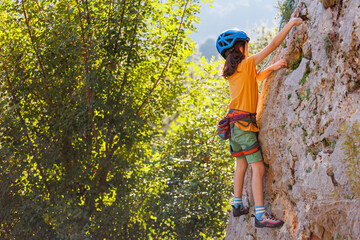 rock climber boy. child is practicing rock climbing. summer camp. sport in nature. cute teenager climbing on a rock with belay