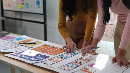Two female designers design creative UX UI screen for mobile responsive application development, developing mockup wireframe on smartphone screen, application development team, brainstorming.