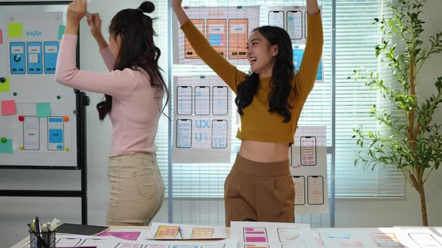 Teamwork. Two female designers working together. UX developer and UI designer at desk in modern office. Happy. Dancing with joy at the finished product. Creativity working on mobile responsive website