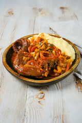 A plate of osso buco with mashed potatoes, onions, and peppers