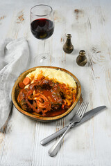 Beef stew with mashed potatoes, onions, and carrots on a white table, with red wine