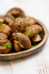 Close-up view of a freshly cooked mushrooms garnished with herbs on a rustic wooden platter