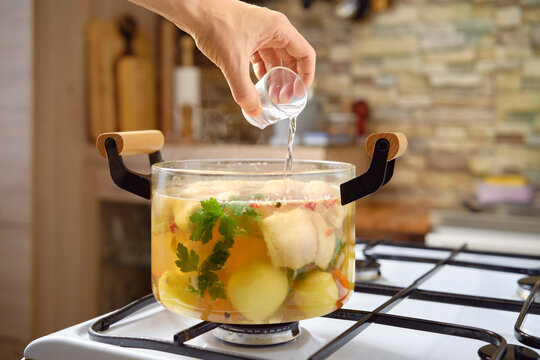 Adding vodka to a flavorful fish soup with vegetable broth and fresh ingredients in a modern kitchen setting
