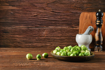Fresh Brussels sprouts in a wooden bowl with kitchen tools against a rustic wooden backdrop