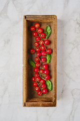 Fresh cherry tomatoes with basil arranged in a rustic wooden box on a marble countertop