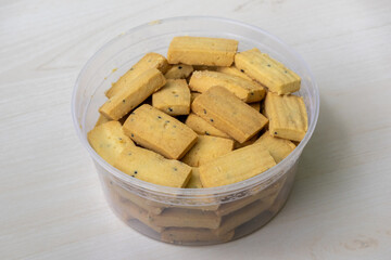 A plastic container filled with soft black cumin biscuits, placed on a wooden surface.
