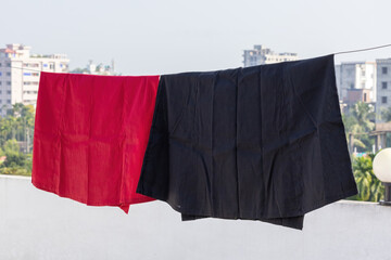 A red and black petticoat hanging on clothesline on rooftop, drying in the sun. Petticoats are traditional undergarments worn by women with sarees or other traditional clothing.