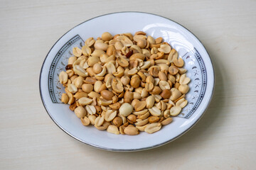 Roasted peanuts (Arachis hypogaea) on a white plate on a light wooden sruface.