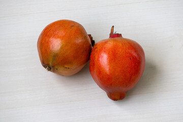 Two ripe pomegranate (Punica granatum) on a light wooden surface.