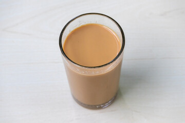 A glass of hot milk tea (dudh cha) on a light wooden surface.