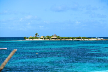 Fototapeta premium Scenic view of a small tropical island surrounded by turquoise waters in Anguilla, featuring lush greenery and thatched huts.