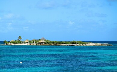 Scenic view of a small tropical island surrounded by turquoise waters in Anguilla, featuring lush greenery and thatched huts.