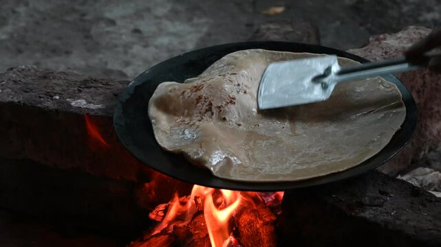 A village woman makes bread on the stove. cooking bread in clay stove , chula , makeing bread , roti , in village