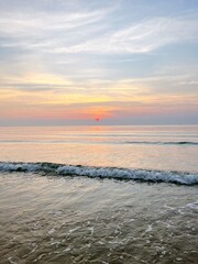 a breathtaking sunset at the horizon of the sea. The sky is painted with hues of orange, pink, and purple as the sun slowly descends, casting a warm glow over the tranquil waters.