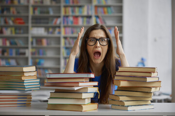 Upset woman screaming sitting front of huge stack of book in library