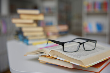 Closeup view on opened paper book with eyeglasses on library table