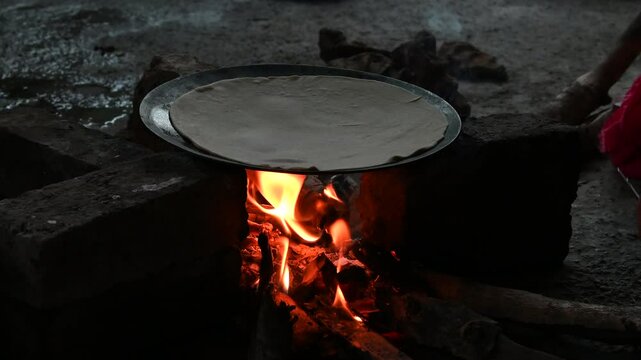 A village woman makes bread on the stove. cooking bread in clay stove , chula , makeing bread , roti , in village