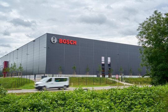 Large industrial BOSCH building, moving vehicle in foreground, surrounded by greenery, depicting corporate architecture and motion. Wernau, Germany, Europe.