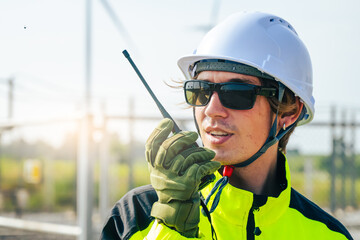 An engineer wearing safety gear closely inspects the base of a wind turbine in a renewable energy field.